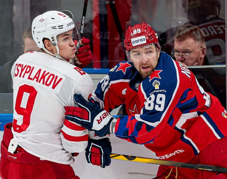 На изображении два хоккеиста в момент силовой борьбы на льду. Один в белой форме с номером 9, другой в синей форме с номером 89. На заднем плане виден тренер или судья у борта