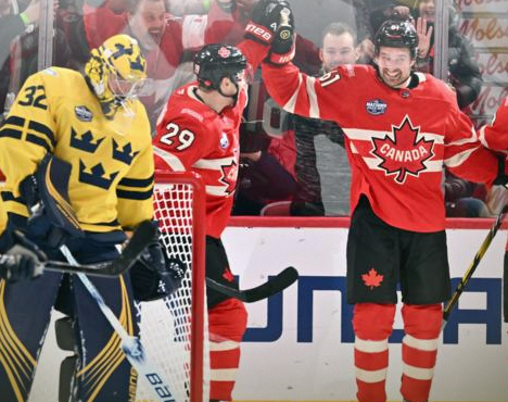 На изображении запечатлён хоккейный матч: игроки в форме сборной Канады празднуют событие, в то время как рядом находится игрок в форме сборной Швеции вратарского амплуа. На заднем плане видны болельщики